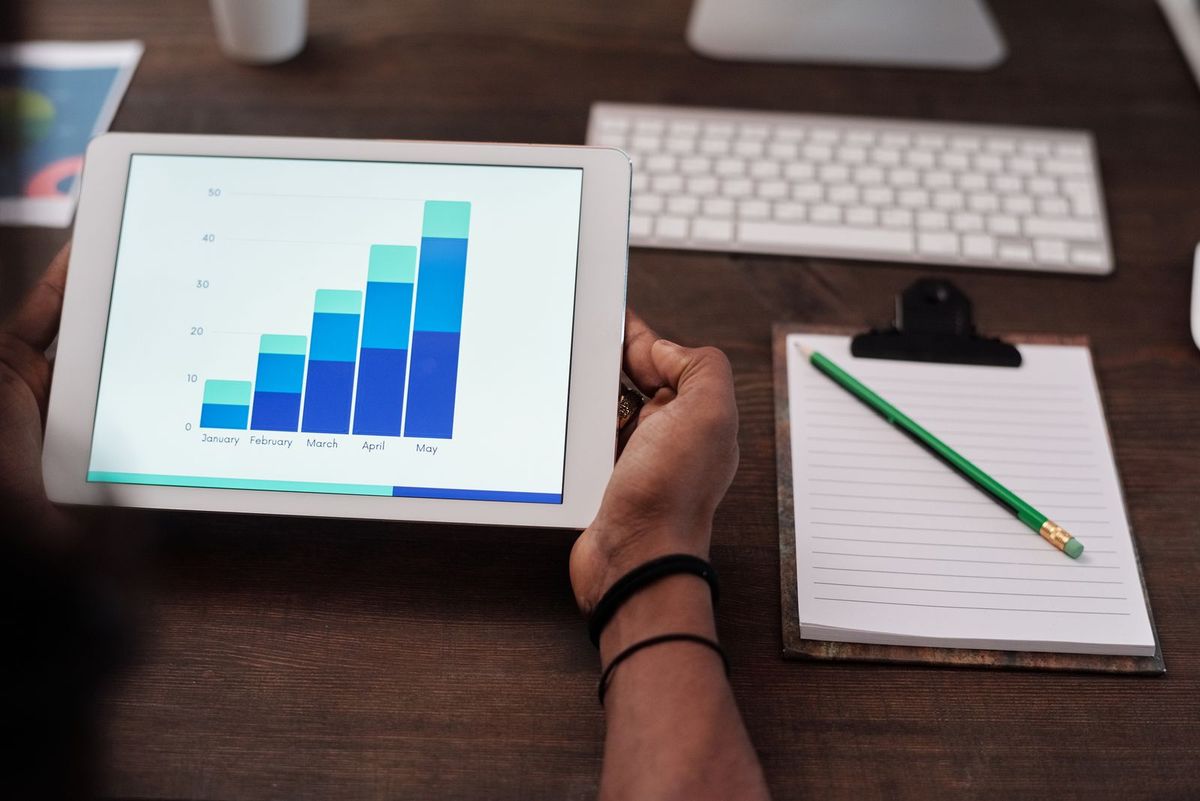 Hands holding a tablet showing a bar chart, with a notebook on the desk