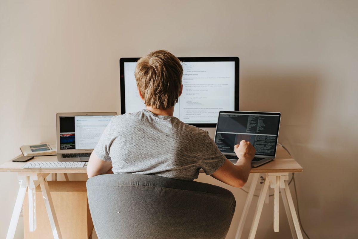 An IT worker at a desk with a monitor and laptop, seen from behind