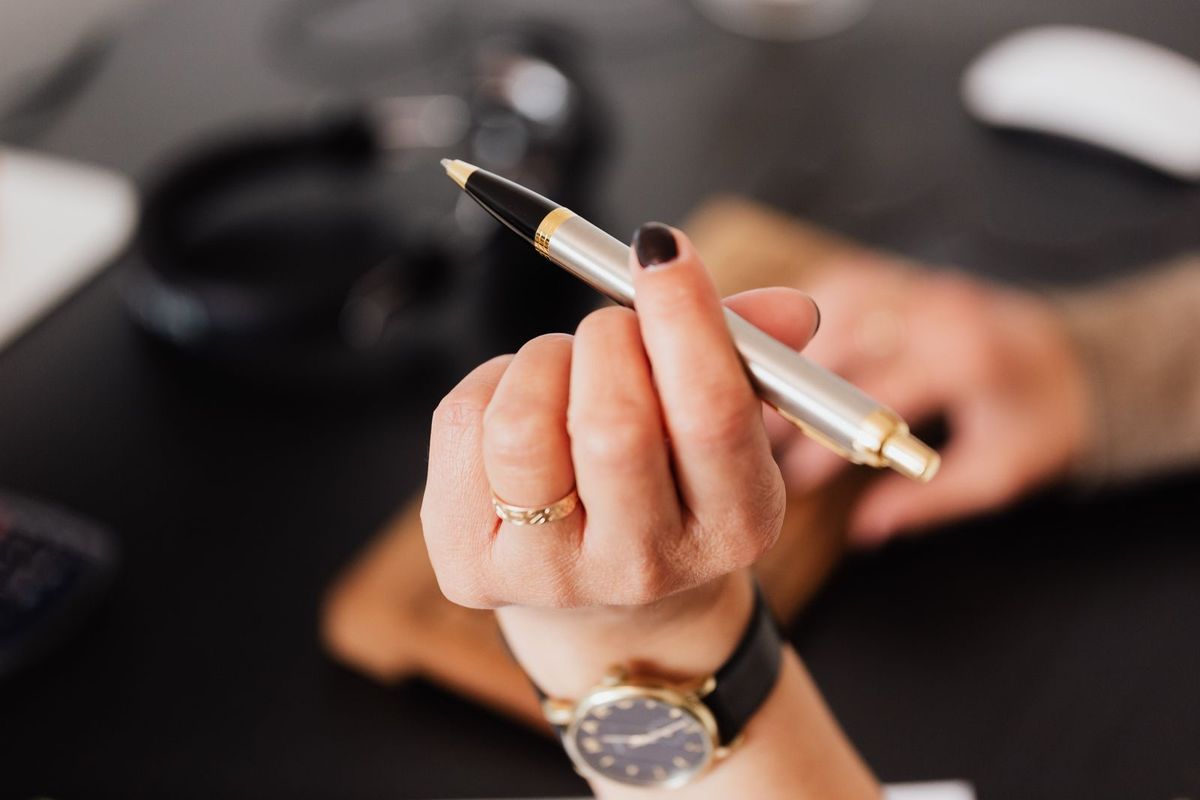 A hand holding a pen over paperwork on a desk