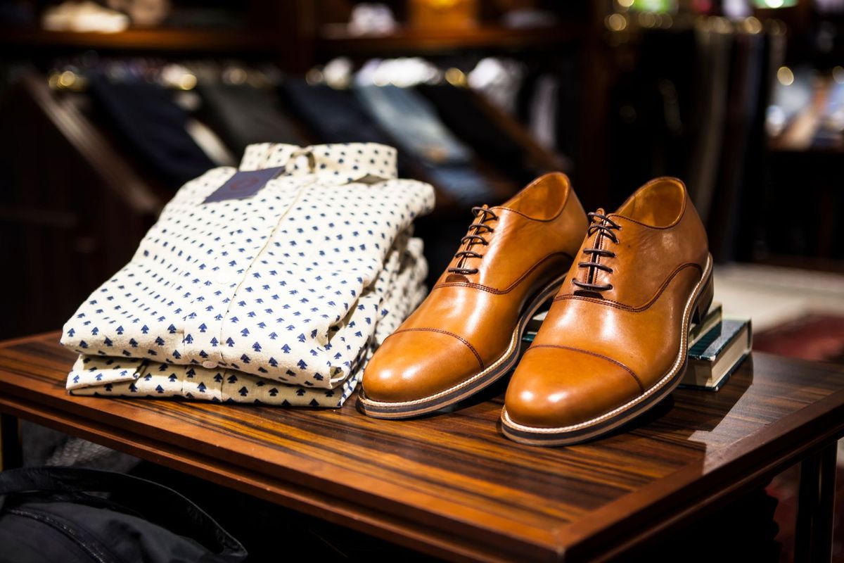 Folded shirts and leather shoes on a display table in a clothing store