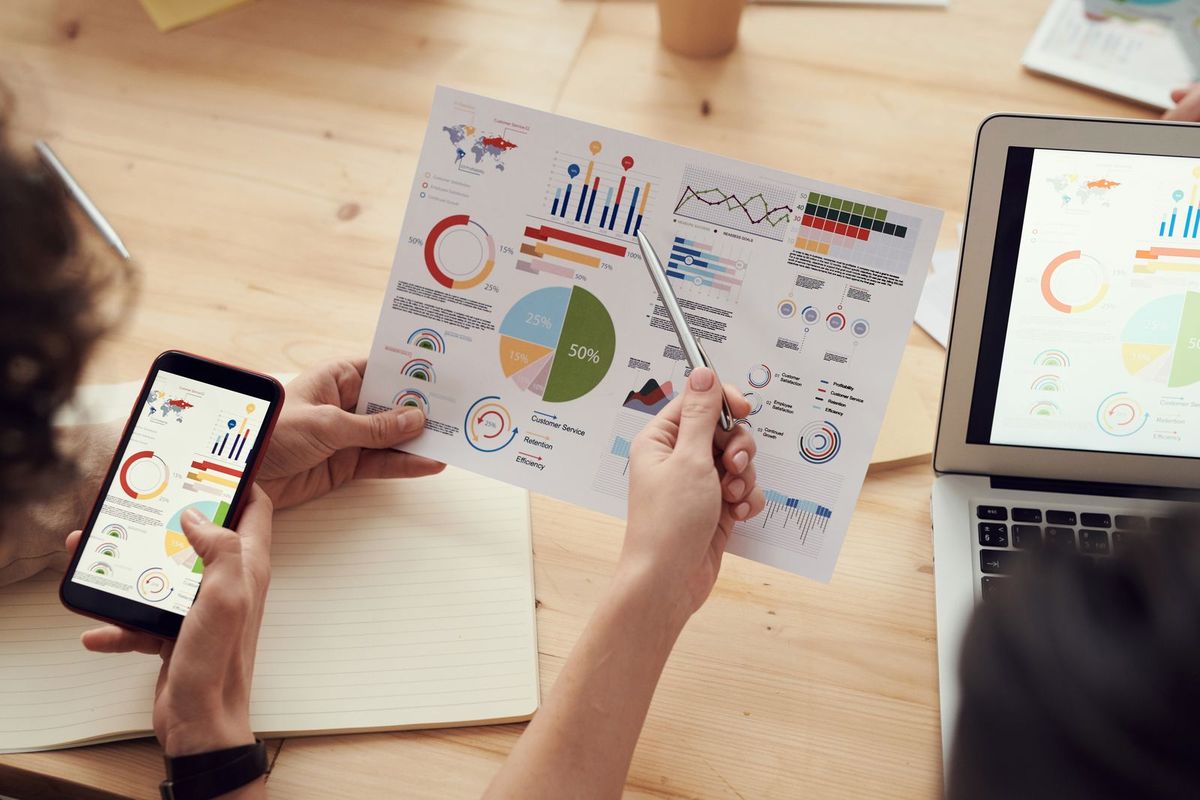 Hands reviewing printed charts and graphs at a table with a laptop